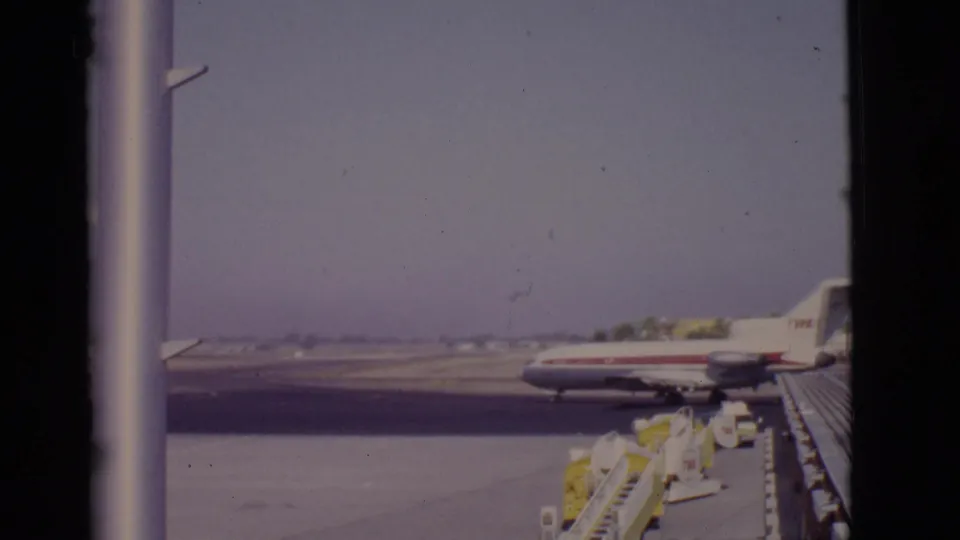Wider 1968 Arizona airport view with a TWA aircraft near the runway and boarding stairs or ramp equipment in the foreground.
