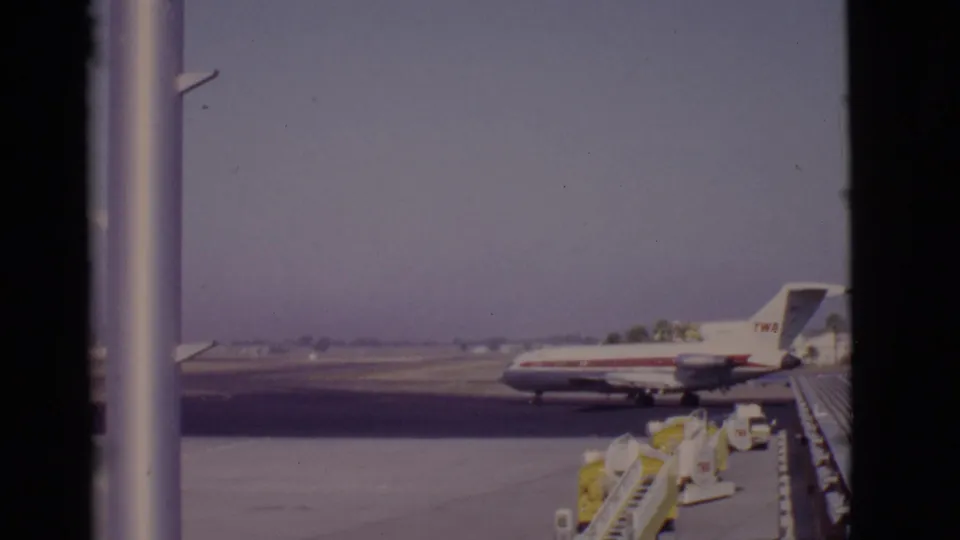 1968 Arizona 8mm frame showing a red-and-white TWA jet on the airport apron, seen through vertical window frames.