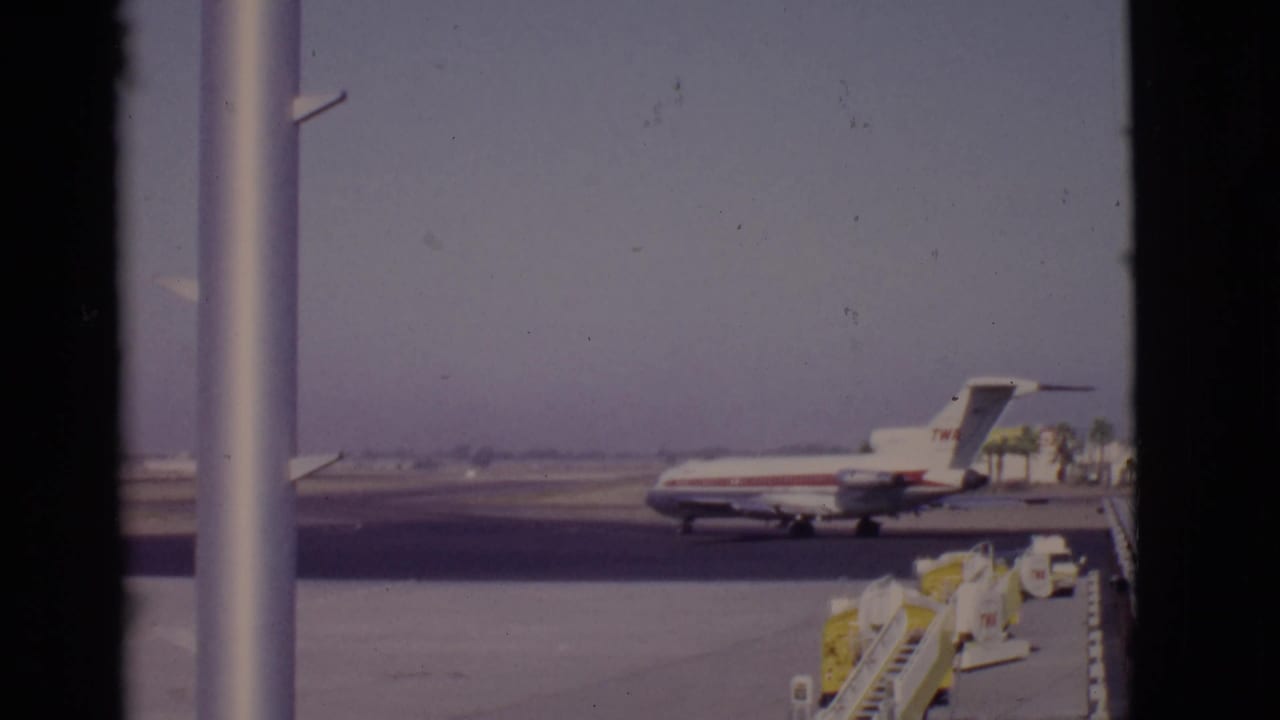 Red-and-white TWA aircraft near ground equipment under a clear sky.