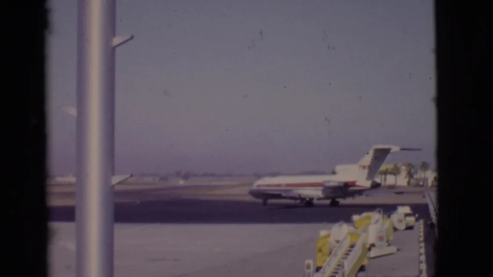The TWA jet remains on the tarmac in this 1968 Arizona airport view, with ground equipment and palm trees in the distance.