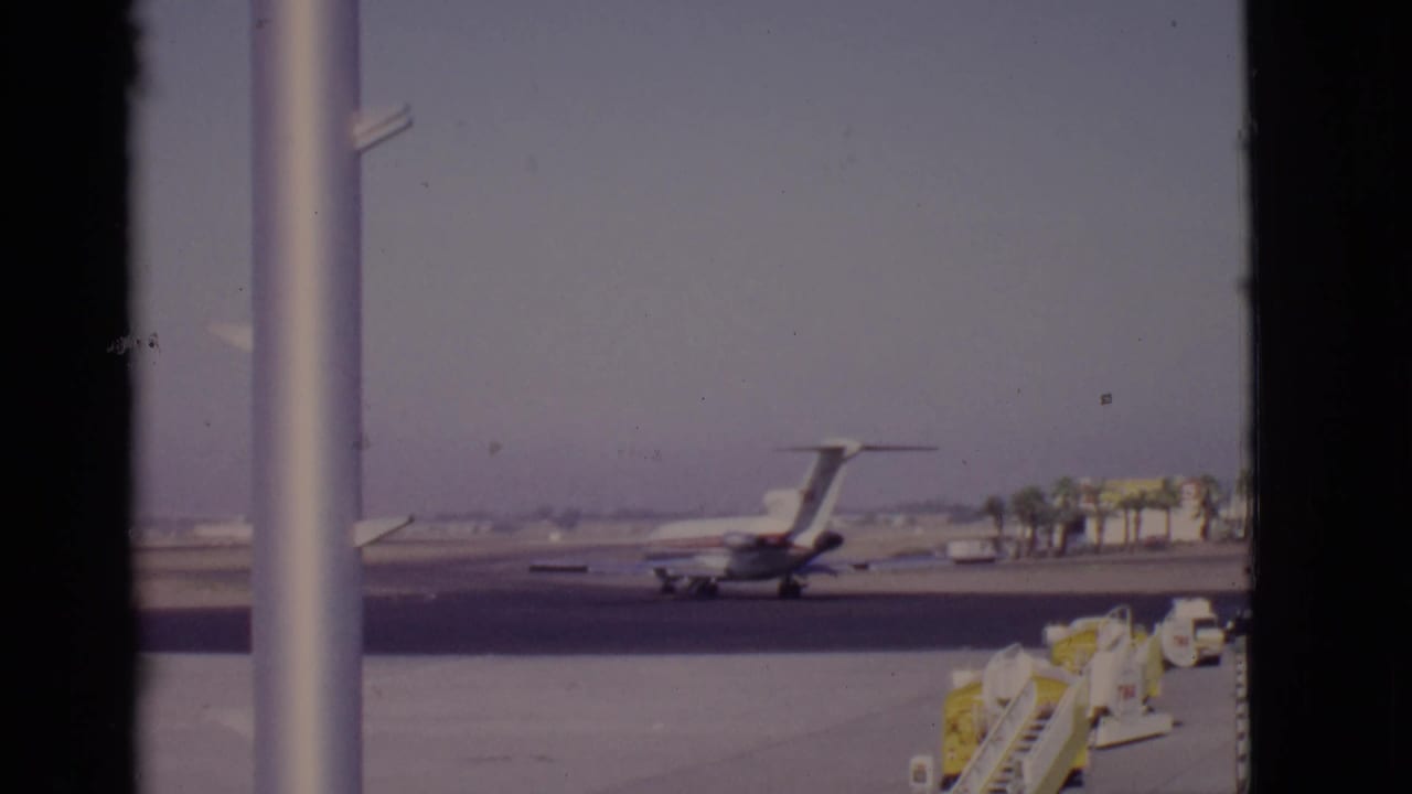 Passenger jet taxiing on a runway seen through vertical window frames.