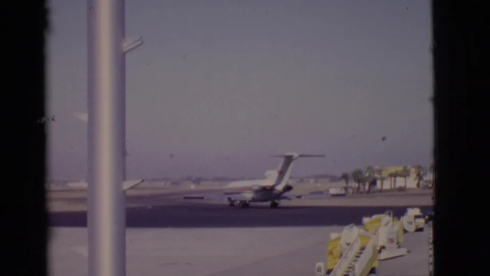1968 Arizona airport view of a passenger jet moving on the runway behind terminal window mullions, with ground equipment nearby.