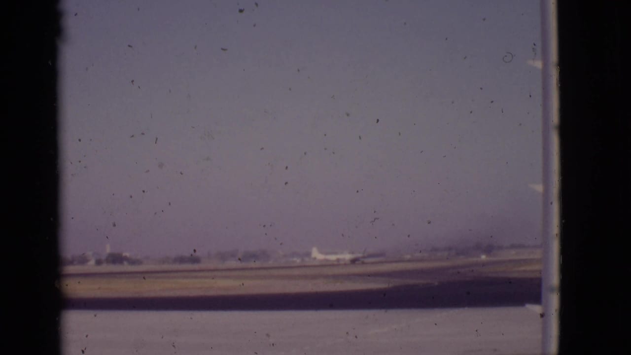 Distant airplane on a runway seen through dark window divisions and 8mm film edges.