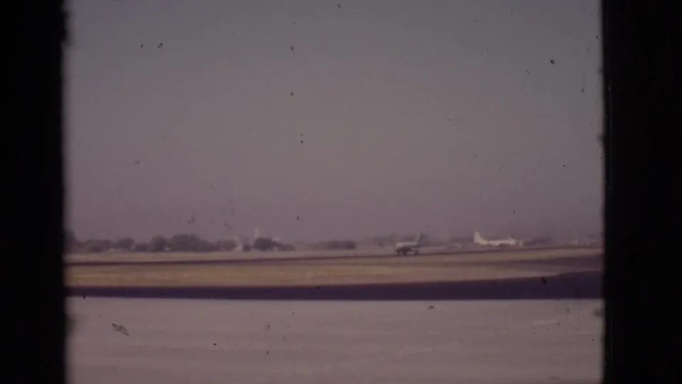 Arizona airport runway scene from 1968 showing a plane near the right side of frame, hazy sky, and window-framed 8mm texture.