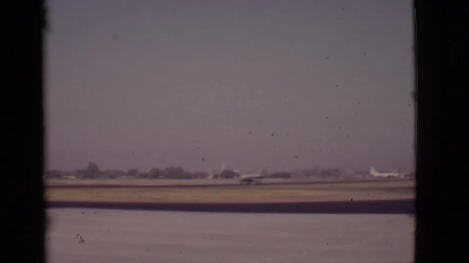 1968 Arizona home-movie frame of a propeller airplane across water on a flat runway, with a hazy treeline in the distance.