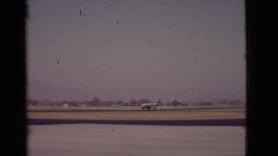 Faded 8mm view from Arizona in 1968 showing a small airplane near a lakeside runway with low trees in the distance.