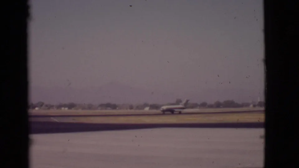 1968 Arizona 8mm frame with a propeller airplane on a runway near water, seen through dark vertical borders and faded color.