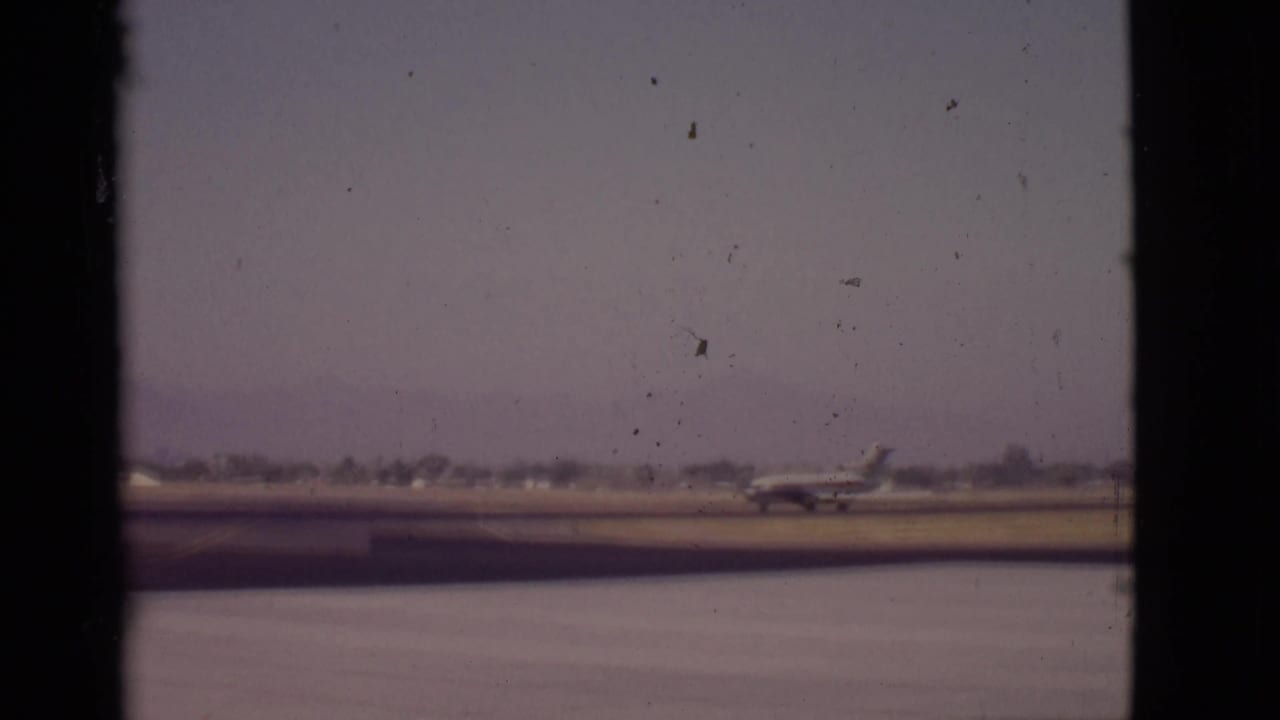 Small passenger aircraft on a runway seen through dark vertical frame edges.