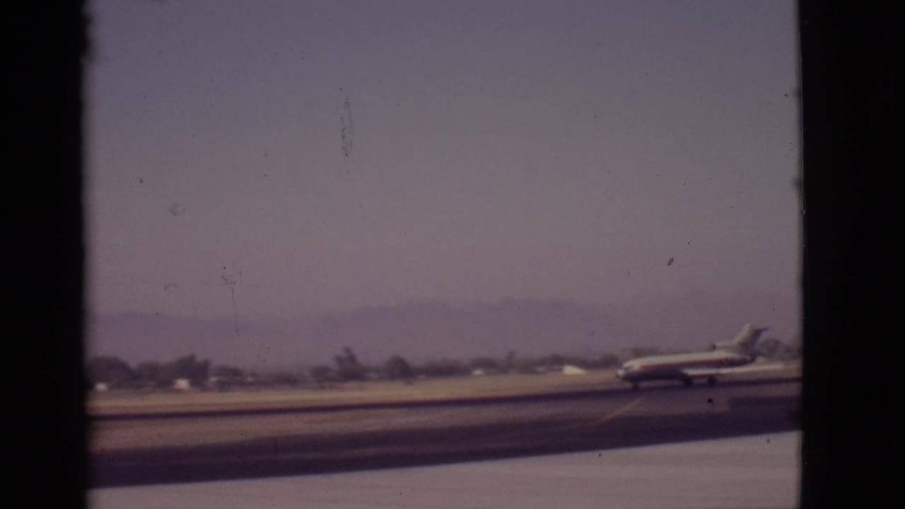 1968 Arizona airport view of a small passenger plane moving rightward on the runway, framed by dark vertical borders.