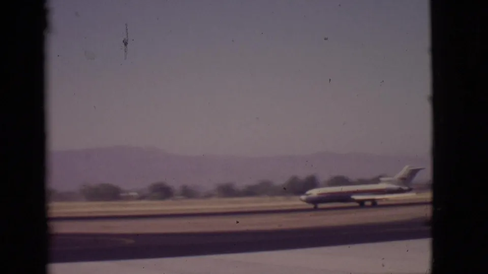 Soft 8mm frame from 1968 Arizona showing the aircraft near the runway edge, with muted sky and mountains behind.