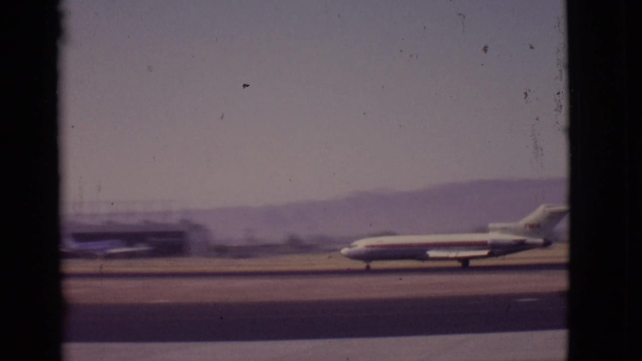 Passenger jet taxiing across a runway behind dark window-frame borders.