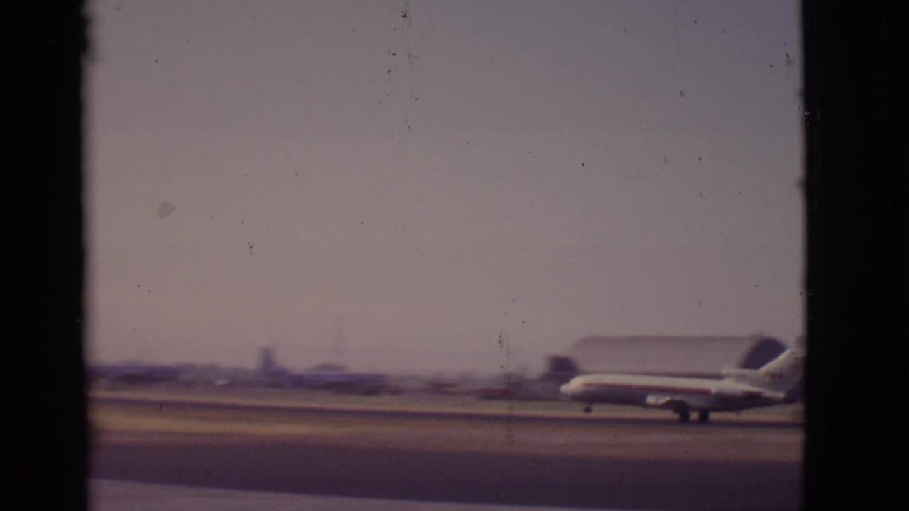 The jet continues along the Arizona runway under a hazy sky, with low airport structures and mountains beyond the tarmac.