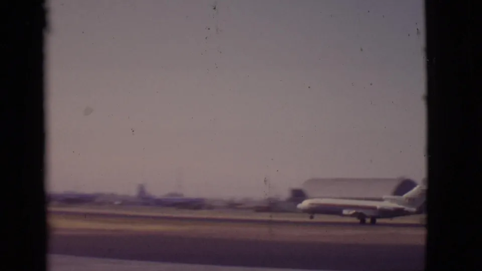 The jet continues along the Arizona runway under a hazy sky, with low airport structures and mountains beyond the tarmac.