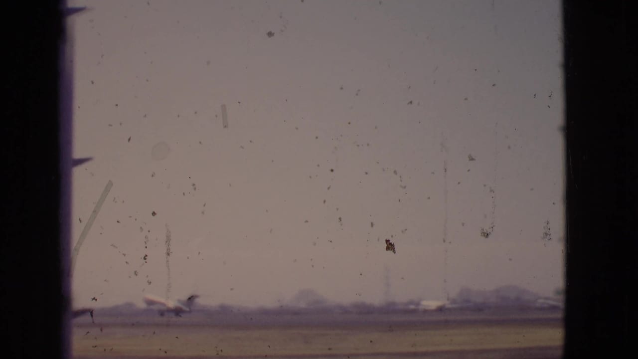 Distant airplane near a runway seen through dark window framing under a hazy sky.
