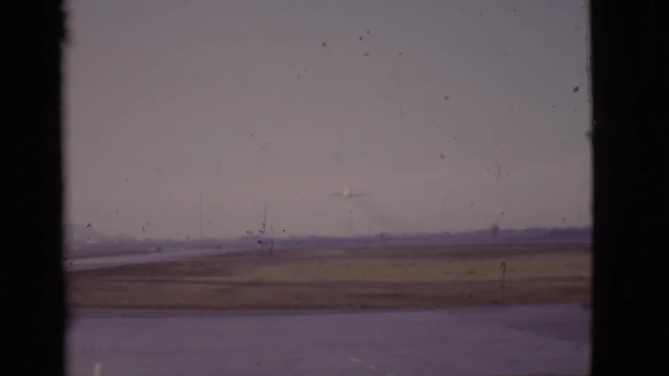 1968 Arizona 8mm frame with a tiny airplane flying beyond the runway, seen through dark window framing and archival film wear.