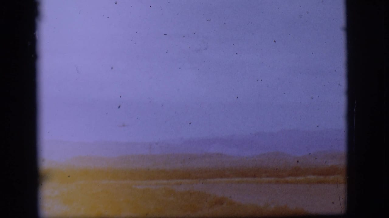 Distant landscape with water, low hills, sky, and dark 8mm frame borders.