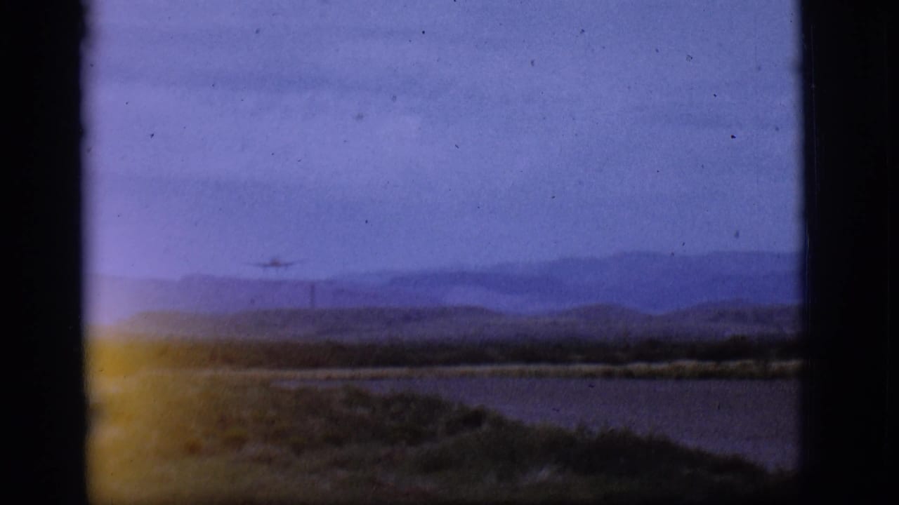 Small jet silhouette descending over a distant runway with hills behind it.