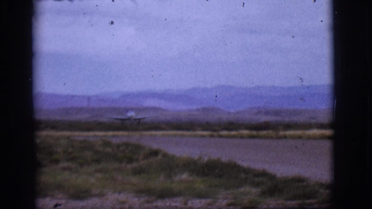 Small propeller plane on a runway with scrubland and distant mountains.