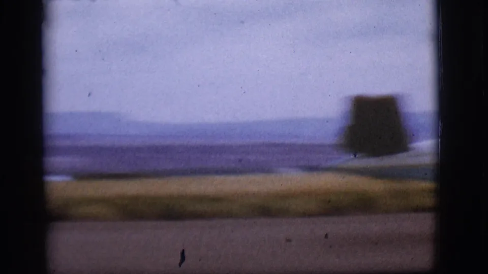 Soft final 8mm frame of the runway landscape near Flagstaff, with distant mountains and a dark out-of-focus shape at the edge.
