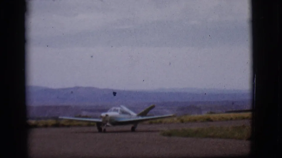 The 1968 Flagstaff footage shows a small single-engine plane closer in frame on the runway, with muted mountains and cloudy sky behind it.