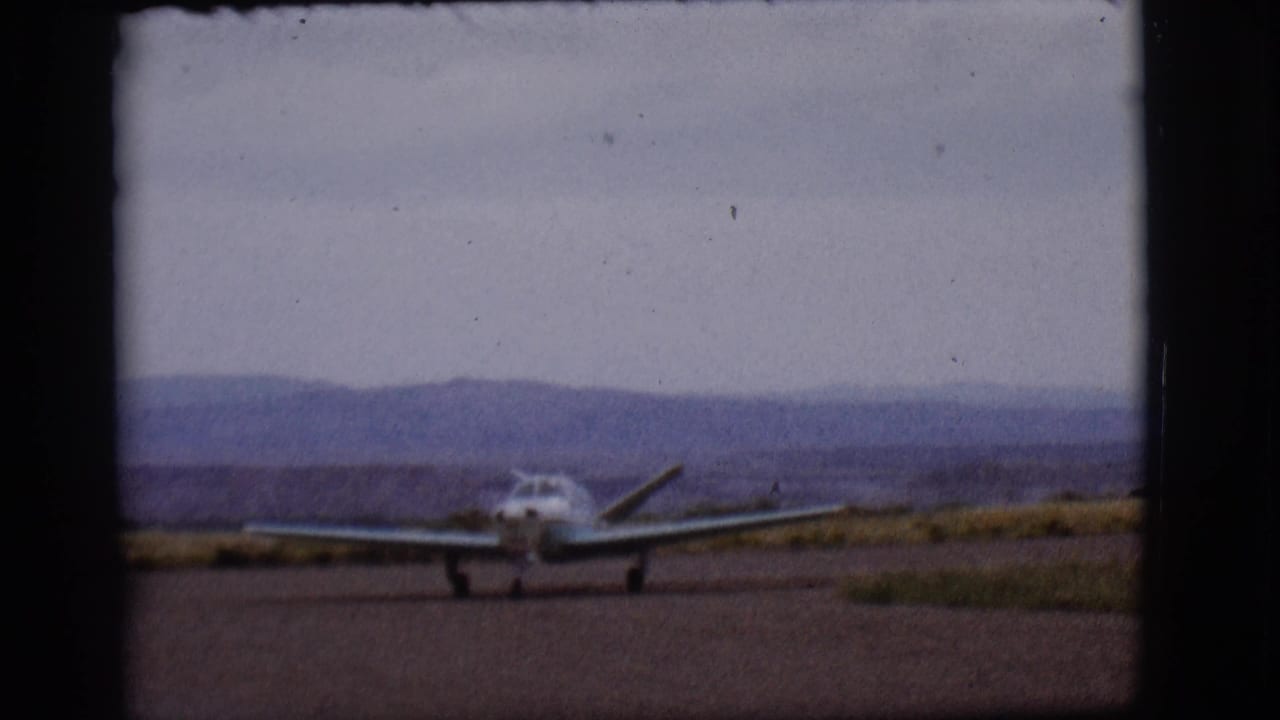 Small single-engine plane taxiing on a runway with distant hills under a cloudy sky.