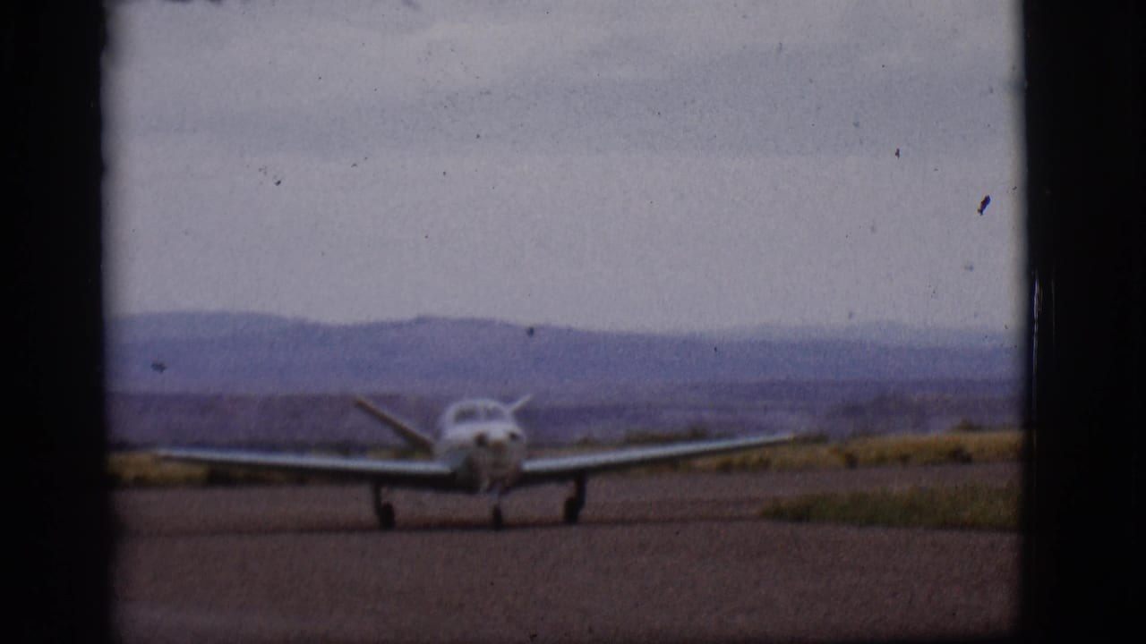 The single-engine aircraft remains centered on the Flagstaff runway, framed by 8mm film edges and a muted mountain horizon.