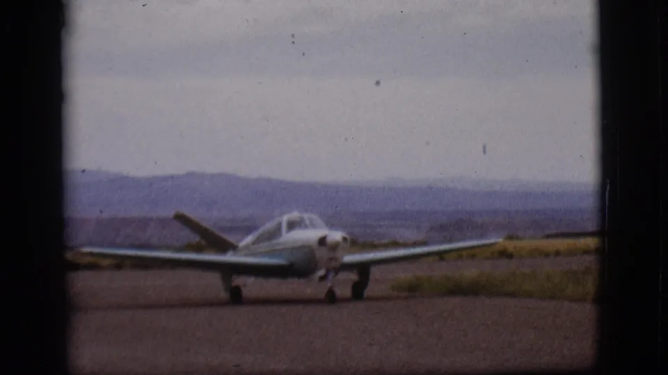 A closer 1968 Flagstaff view shows the small aircraft taxiing forward across the runway with hills and cloudy sky behind.