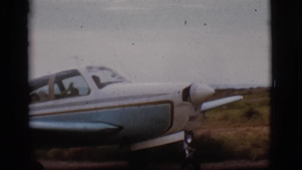 1968 Flagstaff home-movie frame showing a close side view of the small airplane, with possible occupants visible through the cockpit windows.