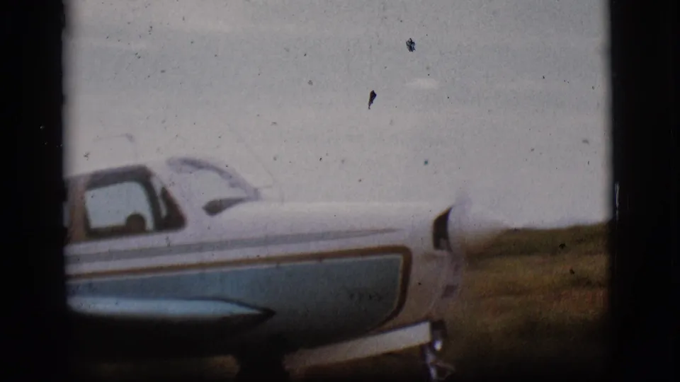 Small blue and white propeller plane on a Flagstaff, Arizona runway in 1968, seen in soft 8mm color from beside the cockpit area.