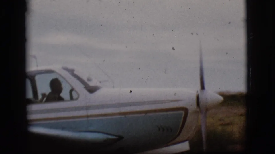 Close side view of the small aircraft cockpit in 1968 Flagstaff footage, with a person silhouetted behind the window.