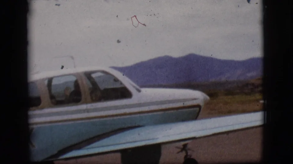 Blue and white light aircraft filmed from the side on a Flagstaff runway, with a wing in the foreground and mountains beyond.