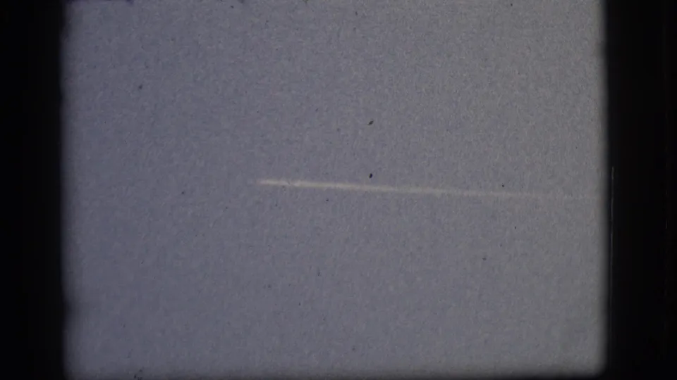 Flagstaff-attributed 1968 8mm frame with a pale horizontal streak across clear sky, bordered by dark film gate edges and speckling.