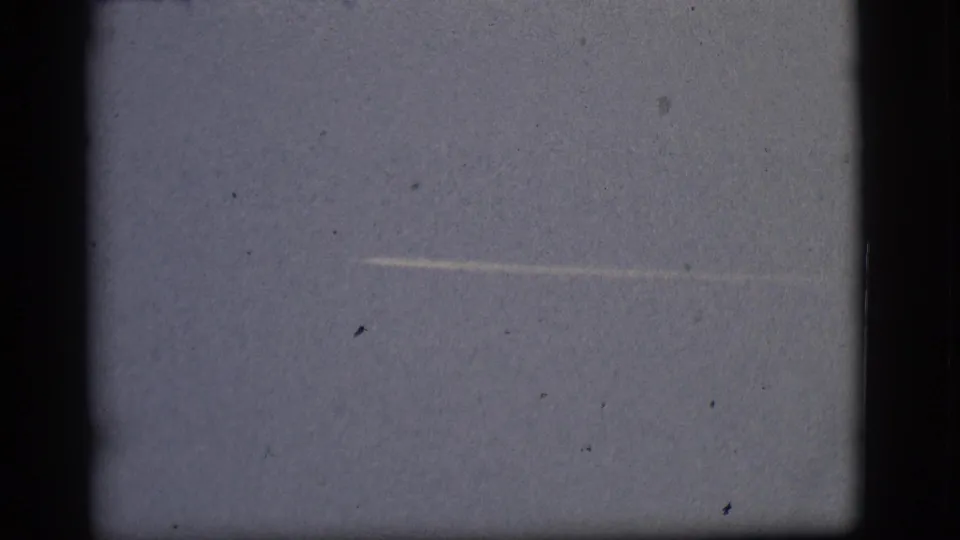 1968 8mm home-movie frame from Flagstaff, Arizona, showing a thin white jet contrail across an open pale blue sky.