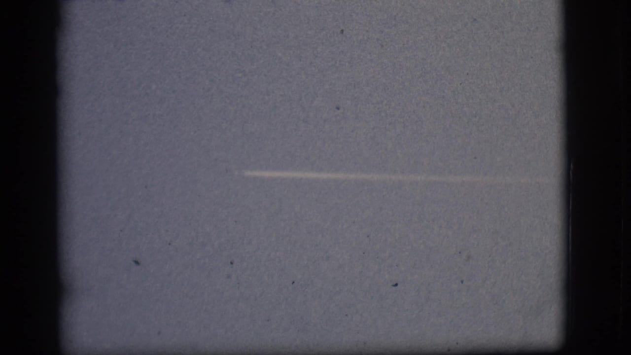 A small distant aircraft and white contrail appear against the Flagstaff sky in this 1968 8mm home-movie frame.