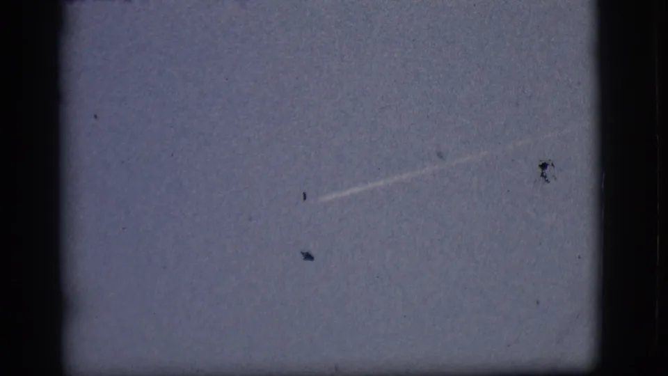 1968 Flagstaff 8mm frame showing a faint white contrail angled across a pale blue sky, bordered by the film gate.