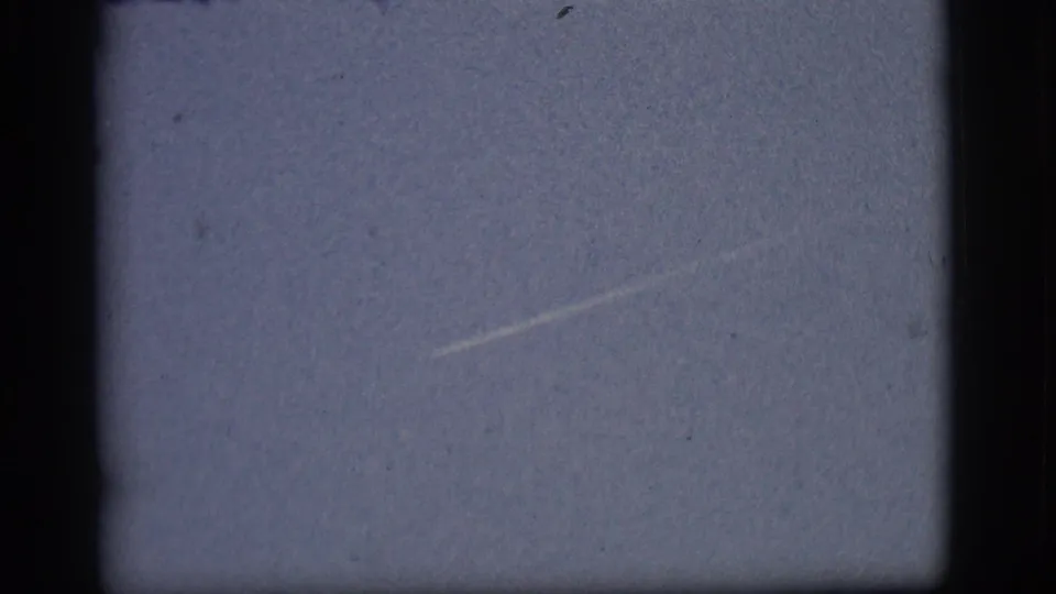 1968 Flagstaff 8mm frame showing the aircraft trail fading diagonally in a pale sky with visible film grain and border edges.