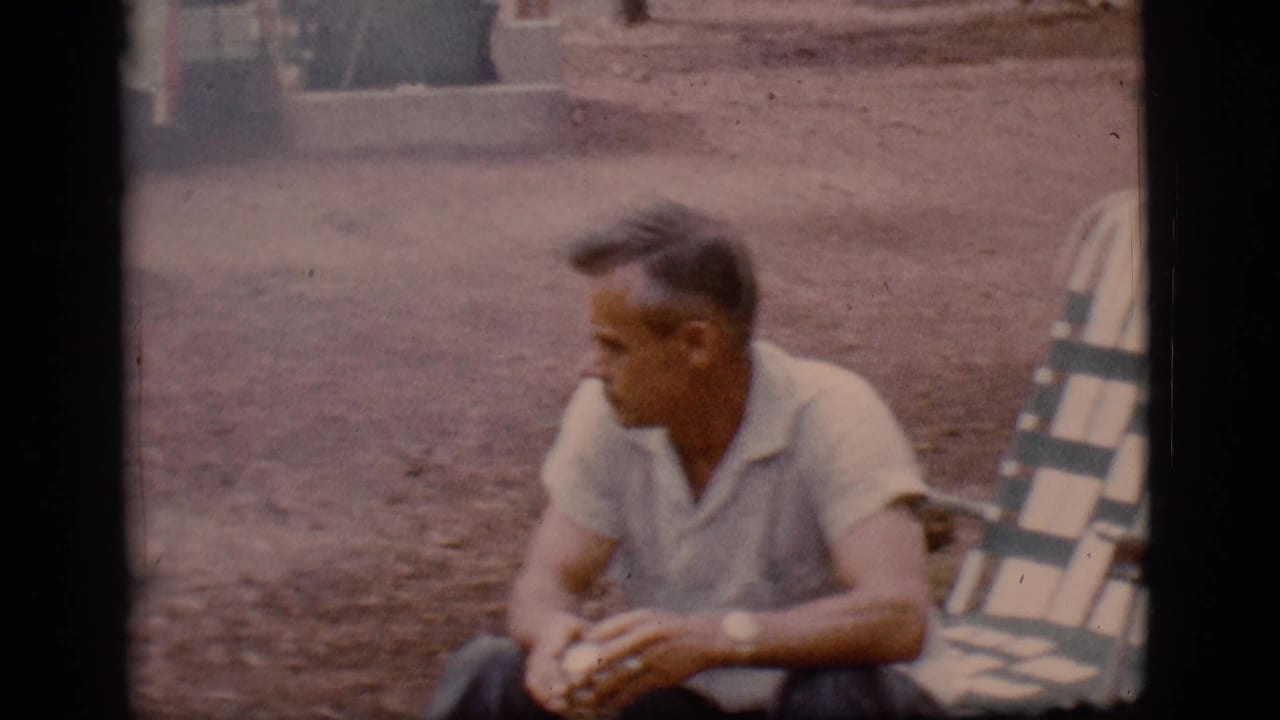 Man seated near a striped folding chair at a campsite.