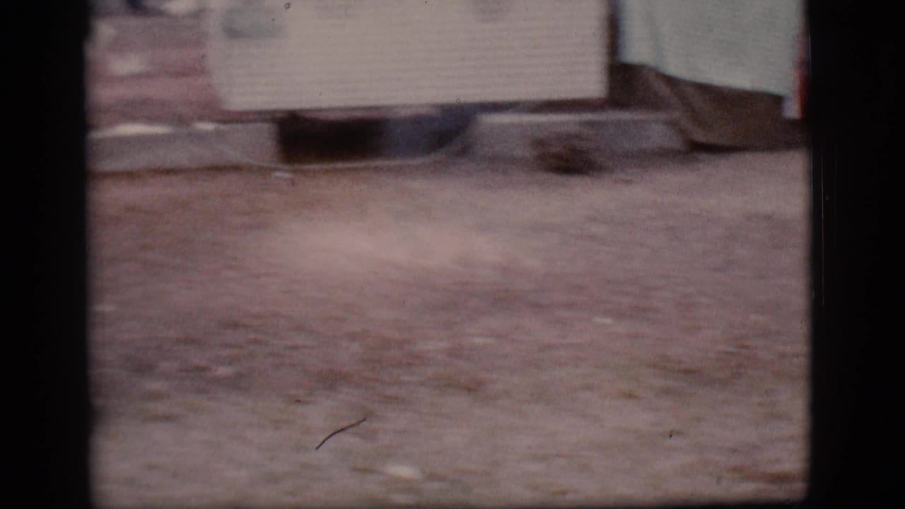 Soft 8mm frame showing dirt ground and the lower edge of a structure or object.
