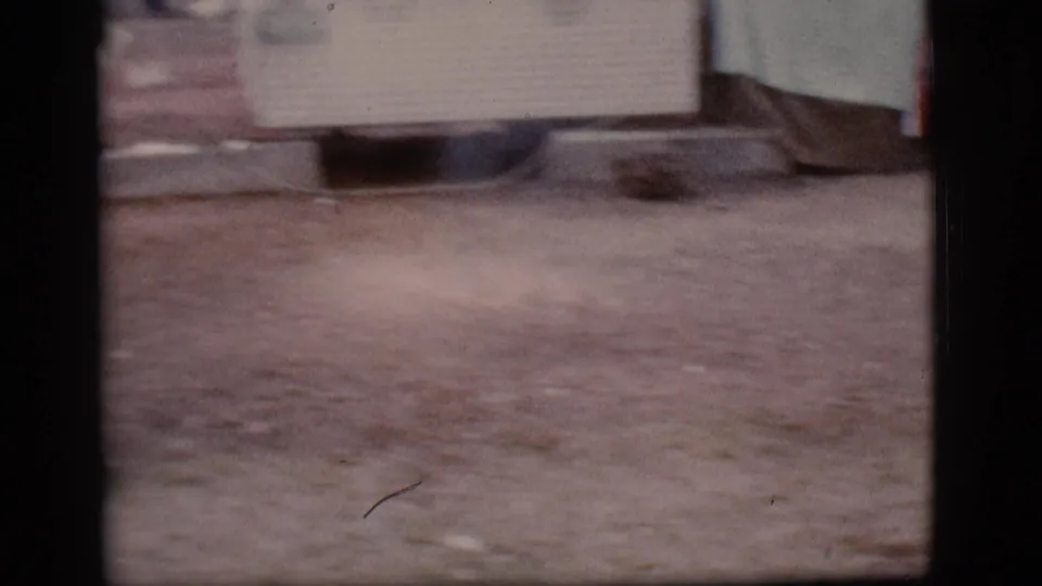 Opening 1968 Flagstaff home-movie frame with soft focus on dirt ground and a partial pale structure or object near the top.