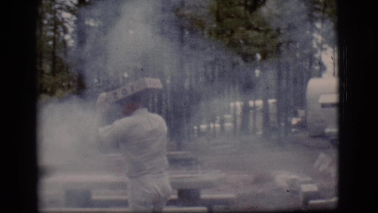 A man in pale clothing tends a smoky fire near picnic tables in wooded Flagstaff, Arizona, in 1968 home-movie footage.
