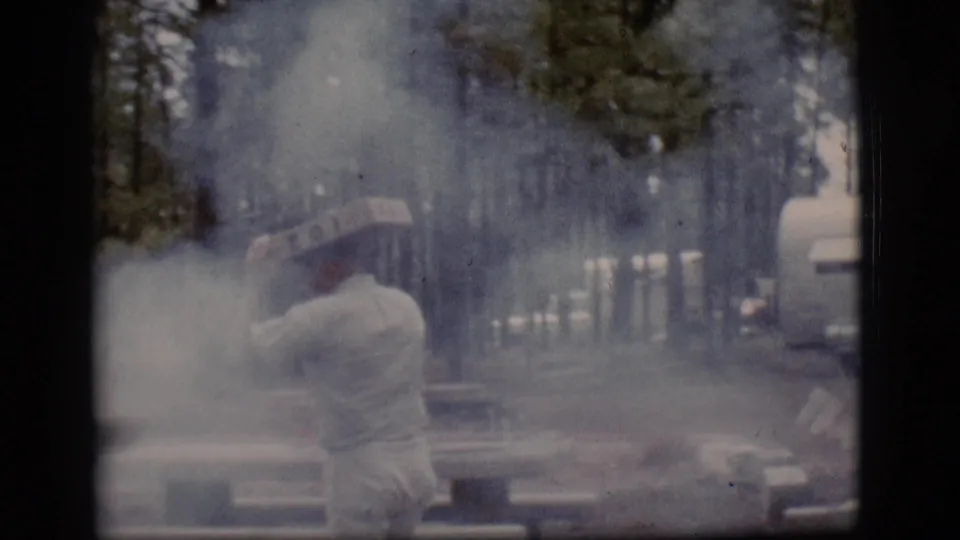 A man in pale clothing tends a smoky fire near picnic tables in wooded Flagstaff, Arizona, in 1968 home-movie footage.