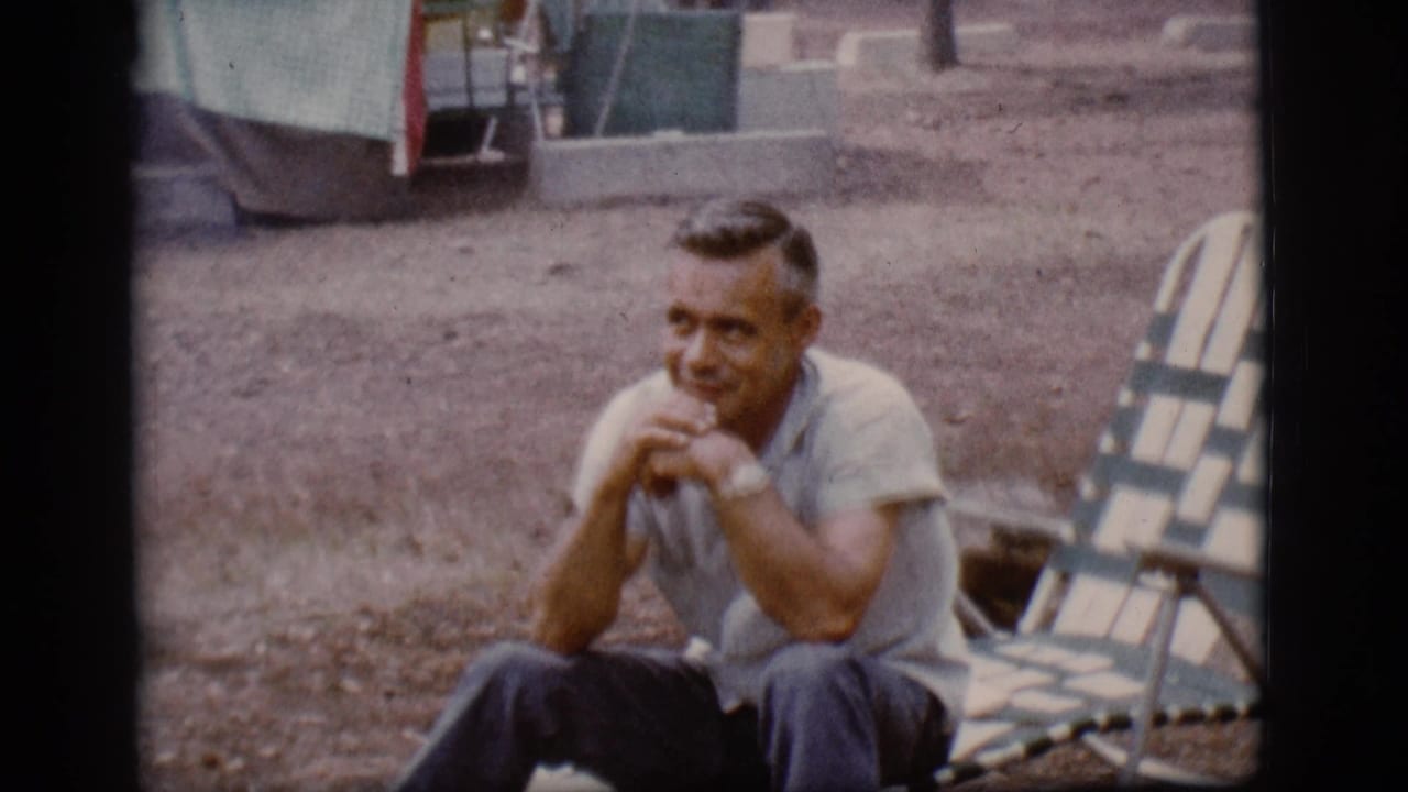 Man seated near a striped lounge chair at a gravel campsite.