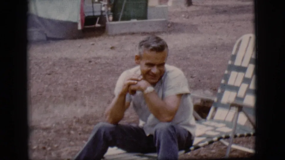 An adult man smiles while seated at a Flagstaff campsite, with a striped folding lounge chair and canvas shelter behind him.