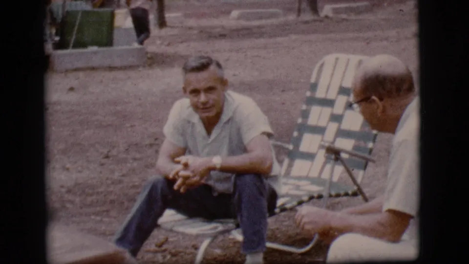 1968 Flagstaff home-movie view of two men in folding chairs on dirt ground, with a green trash can in the background.