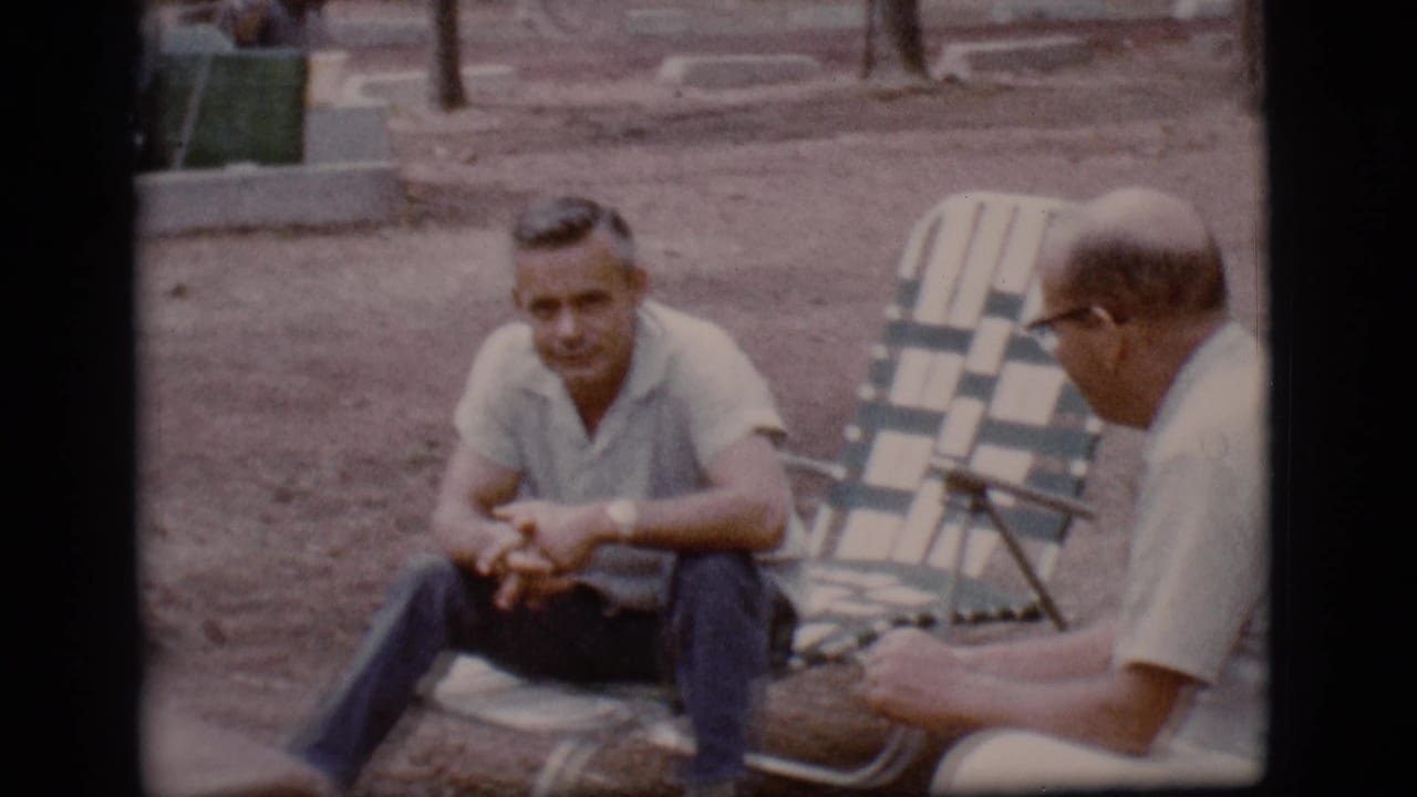 At the Flagstaff campsite, one man looks forward while his companion in glasses sits nearby on a folding chair.