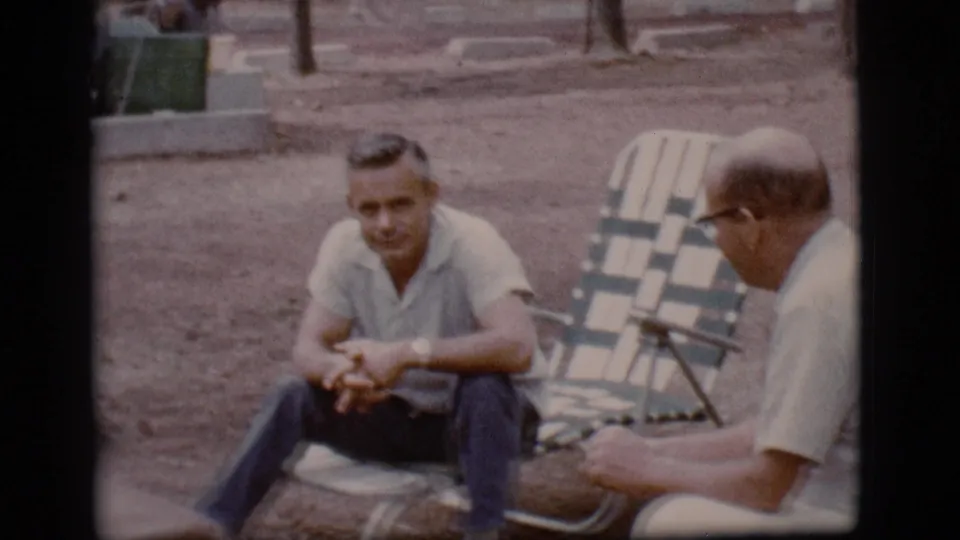 At the Flagstaff campsite, one man looks forward while his companion in glasses sits nearby on a folding chair.