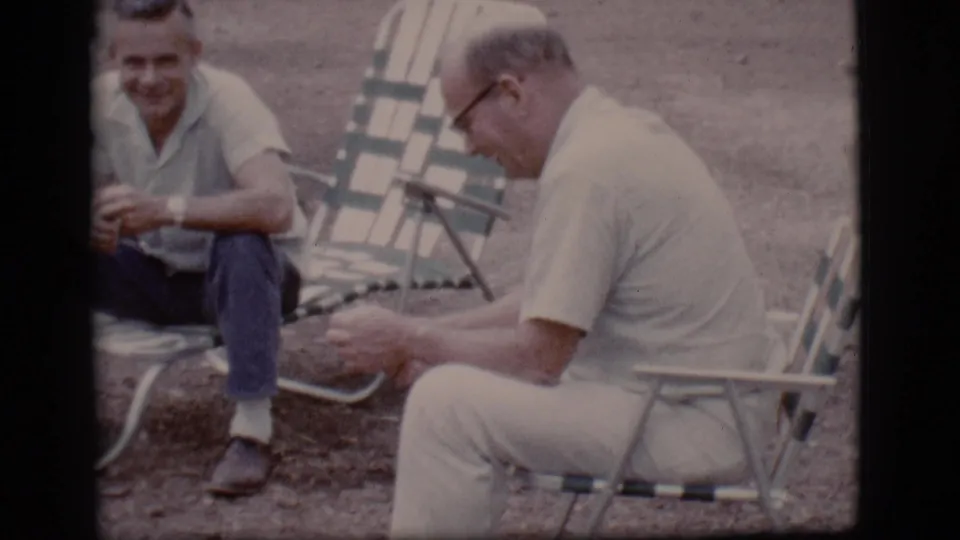 At the end of the clip, the man in glasses sits in profile on a lawn chair while his companion smiles nearby.