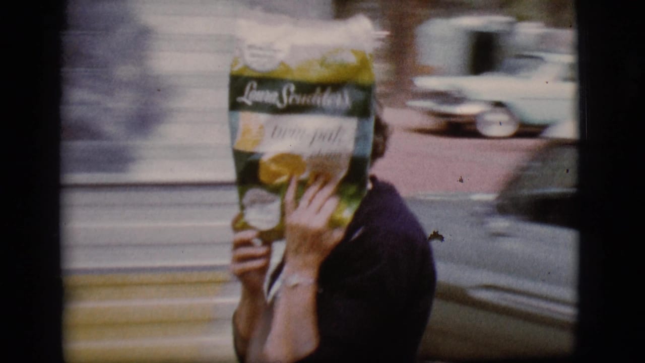 Woman holds a grocery bag in front of her face beside a camper trailer.