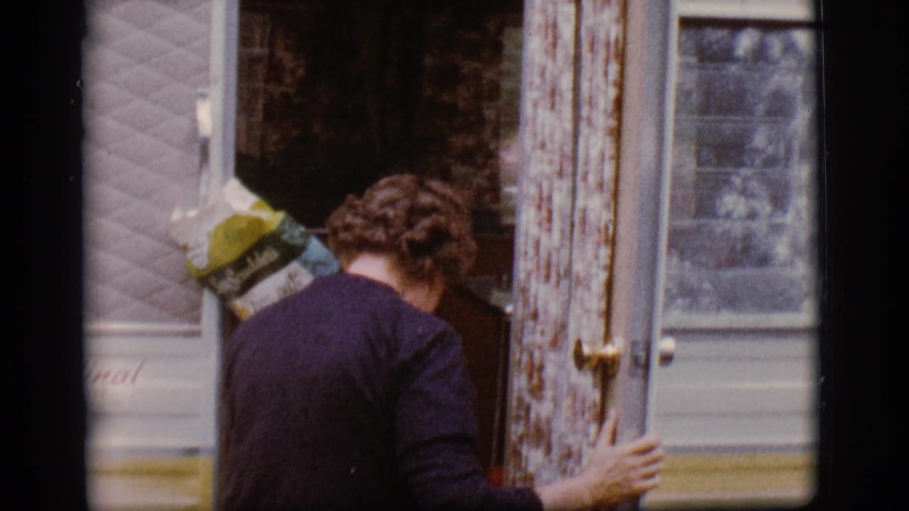 Woman carrying a grocery bag enters the open doorway of a camper trailer.