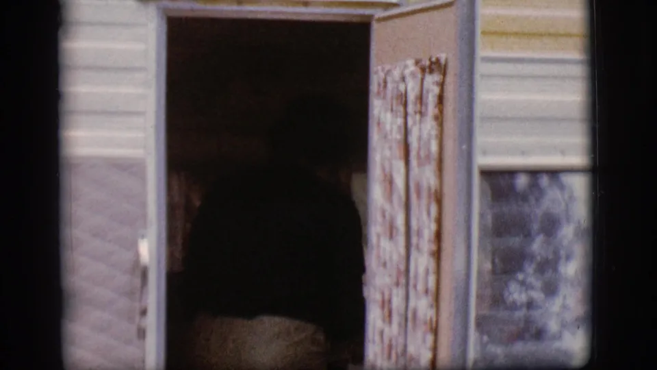 The camper doorway stands open, showing a dark interior, patterned curtain, exterior siding, and nearby window in the 1968 travel scene.
